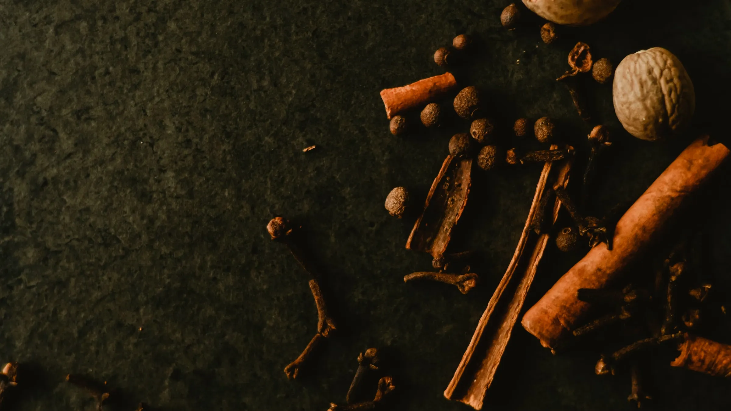 Cinnamon, cloves, nutmeg, and pepper on dark slate