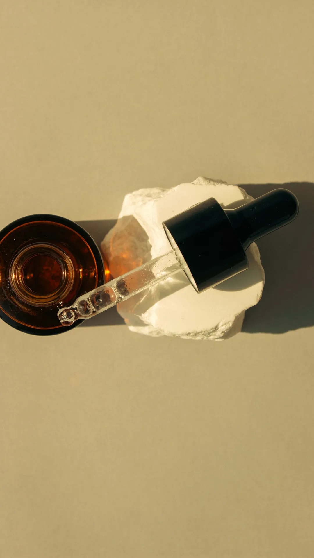 Dropper and dark oil bottle on plaster, seen from above